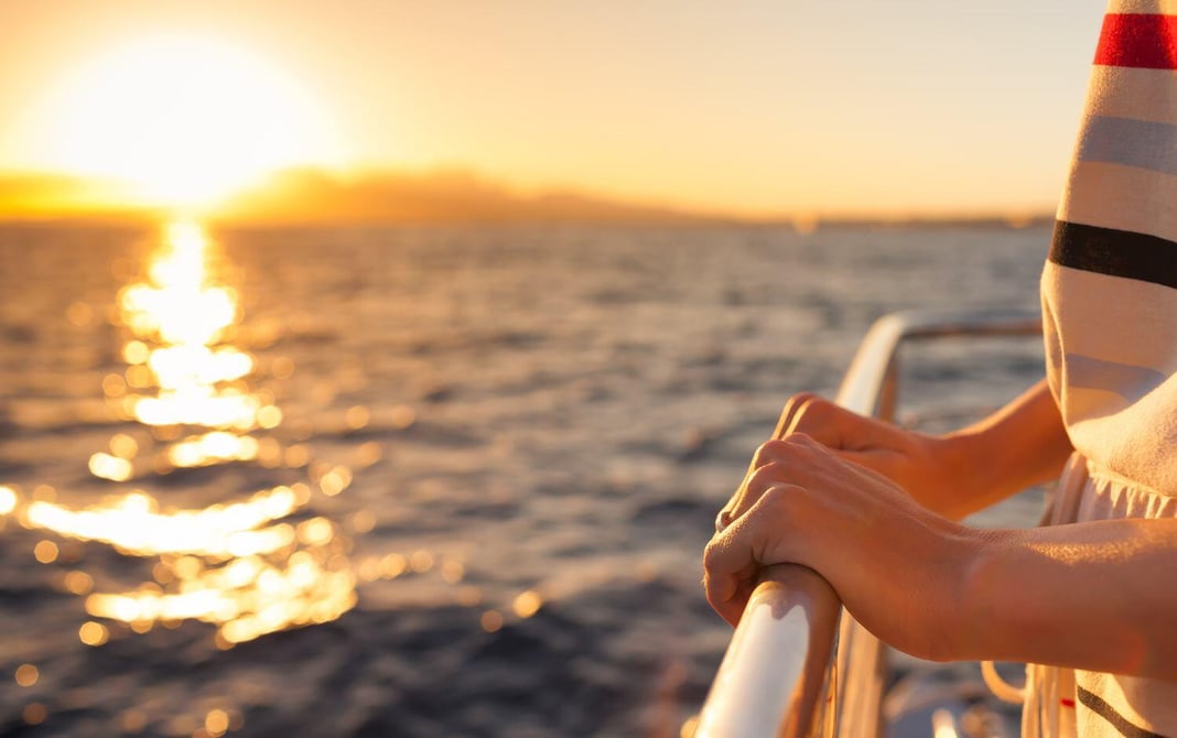 A view of the sea at sunset someone is holding the railing of a cruise ship